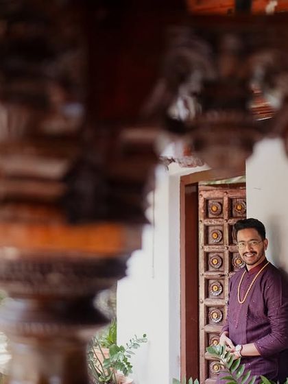 A groom, seen through the intricate carvings of a wooden pillar, waits in the courtyard.