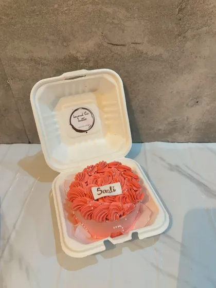 A pretty pink bento cake with a rosette piping design, customized with the name "Saali" on a small plaque.