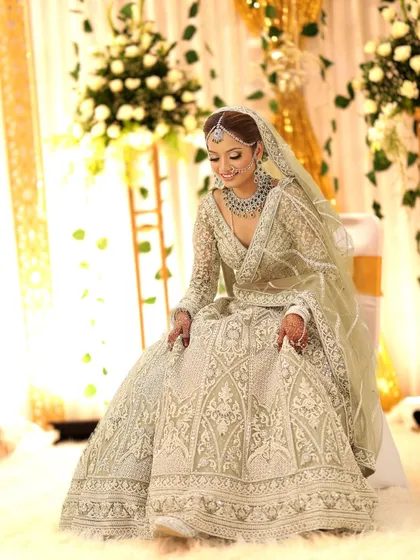 A full-length shot of the bride seated, showcasing the beautiful drape of her lehenga and the elegance of the full diamond jewellery set.