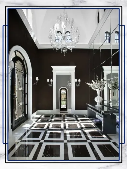 This grand foyer showcases a bold black and white marble floor pattern, complemented by a crystal chandelier and high ceilings, creating an unforgettable entrance.