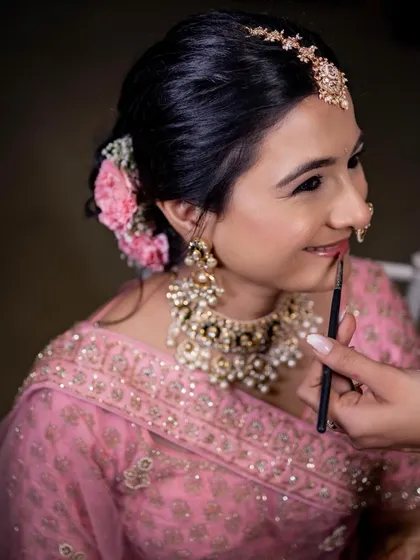 A behind-the-scenes moment, adding the final touches to this bride's simple and elegant phera look. The focus was on clean skin and soft pink tones.