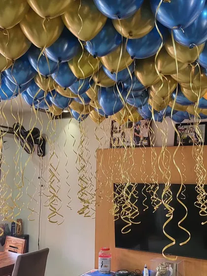 A room ceiling covered in blue and gold helium balloons with dangling ribbons for a festive party atmosphere.