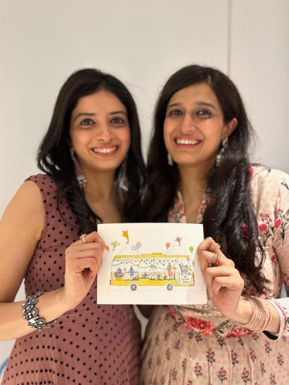 A picture of us, Kamakshi and Vishala, holding a beautiful illustration of our 'Sound Space on Wheels' bus. This drawing captures the heart of our fundraiser and our mission to bring music to all.