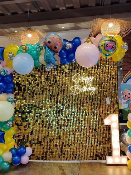 A Cocomelon first birthday party with a gold sequin backdrop. The bright balloons and light-up number '1' make the setup pop.