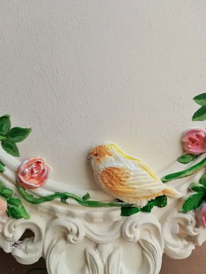 A detailed close-up of the hand-painted bird on the floral wooden frame. I focus on getting the small details right to make each element, like this little yellow bird, come to life.