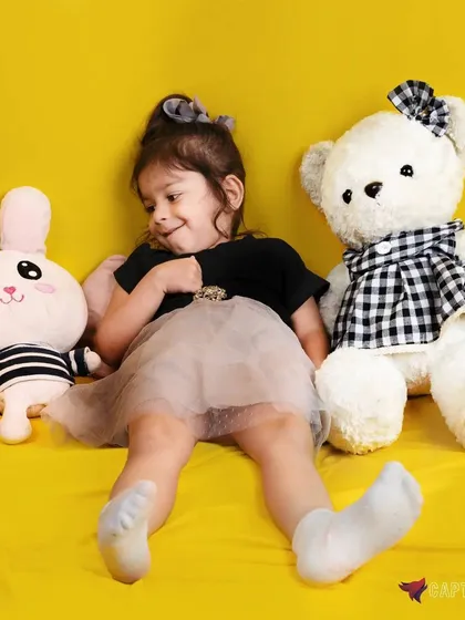 A candid and adorable moment captured in the studio. The young girl is surrounded by stuffed toys, creating a sweet and playful scene that feels natural and full of personality.