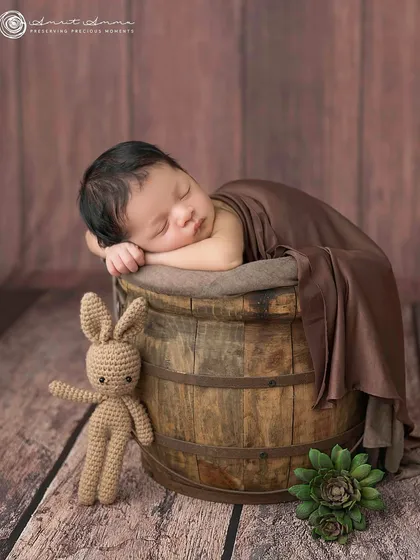 A classic and rustic newborn pose. The baby is nestled safely in a wooden bucket, creating a timeless portrait with beautiful, earthy tones.
