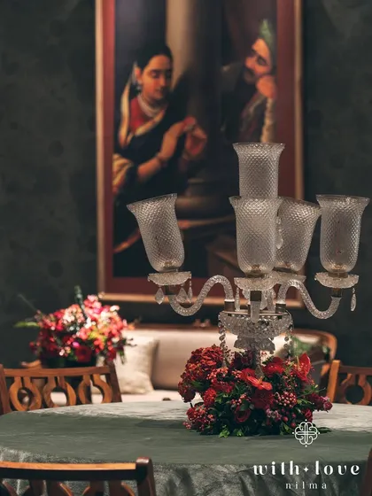 A candelabra centerpiece on a velvet-draped table, with a Raja Ravi Varma painting creating a stunning backdrop. The play of light and shadow is central to the design.
