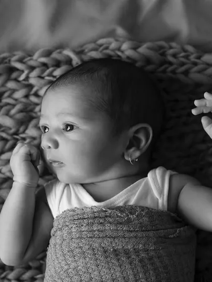 A thoughtful moment captured in black and white. This baby is lying on a chunky knit blanket, looking off to the side with a curious expression.