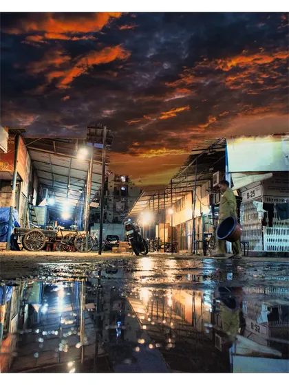 We find beauty in the chaos of everyday life, like this scene from Delhi's Phool Mandi at dusk. This image uses the wet ground to create a stunning reflection of the dramatic orange sky and market lights, turning a simple street scene into a piece of art. This is an example of our creative street photography and post-processing skills.