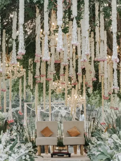 An intimate and elegant mandap setup nestled in a natural, green environment. We used cascading strings of tuberose and blush pink florals to create a delicate curtain, perfectly framing the couple's seating and blending seamlessly with the outdoor wedding theme.