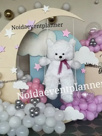 A dreamy 'Over the Moon' theme with a teddy bear on a moon swing, surrounded by balloon clouds in pink, blue, and silver.