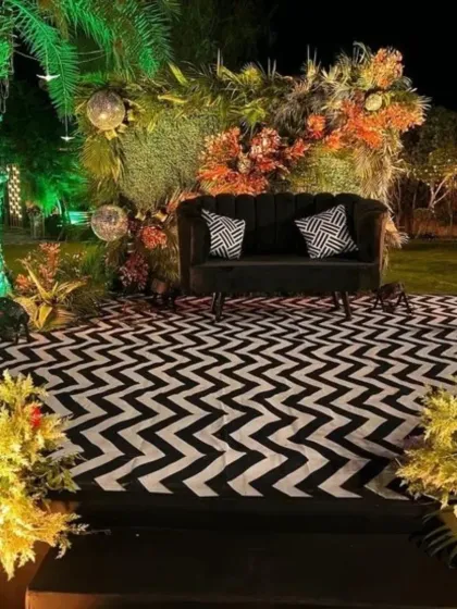 A chic photo-op spot for a Sangeet or cocktail party. The black velvet sofa is set against a backdrop of lush greenery and a modern black-and-white patterned floor.