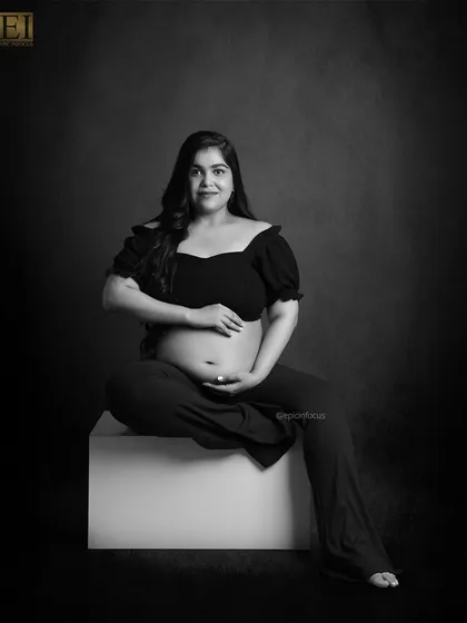 A modern and confident black and white portrait of a mom-to-be seated in a relaxed, cross-legged pose.