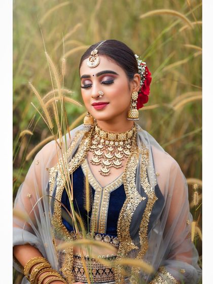 An outdoor bridal shoot capturing a serene and elegant moment. The natural setting complements the traditional lehenga, and the soft lighting highlights the delicate details of the fabric and embroidery.
