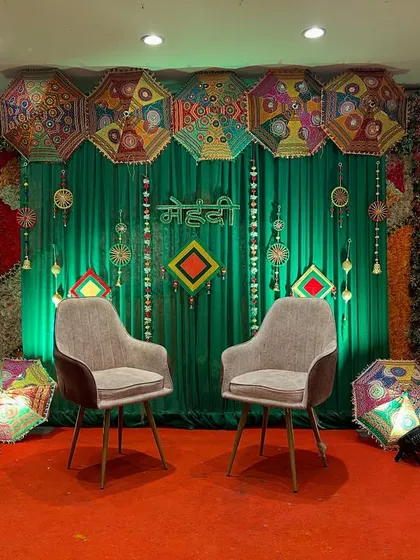 A Mehendi stage setup with a green backdrop, floral walls, and modern chairs, offering a contemporary twist on traditional decor.