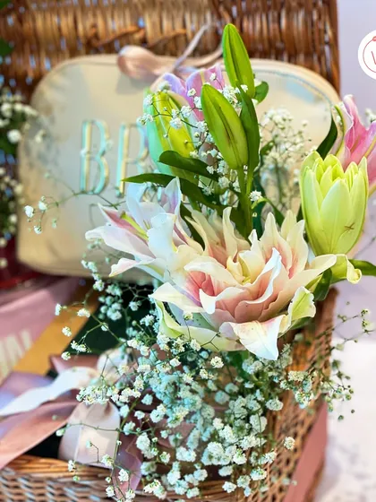 A detail shot showing the personalized "BRIDE" pouch included in our wicker basket hamper, surrounded by fresh flowers.