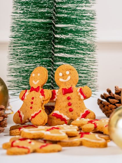 A pair of our festive gingerbread men cookies, standing in a winter wonderland scene.