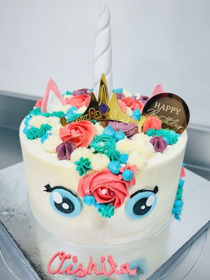 A cute and colorful unicorn cake for a magical birthday. This design features big cartoon eyes, a golden horn, and a mane made of vibrant buttercream rosettes.