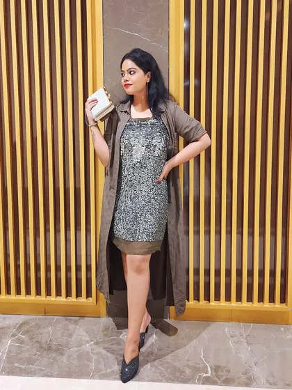 A sequined dress layered with a long, earthy-toned shrug creates a glamorous yet relaxed evening look.