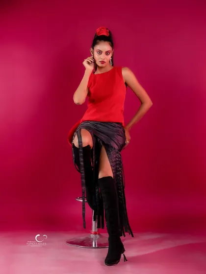 A classic fashion pose on a stool that is both chic and sophisticated. Her gaze is direct and confident.