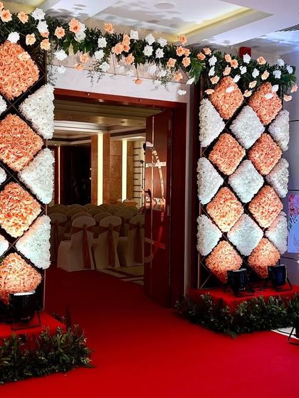 A full view of the entrance with floral cushion pillars, leading guests down a red carpet into the main event hall.