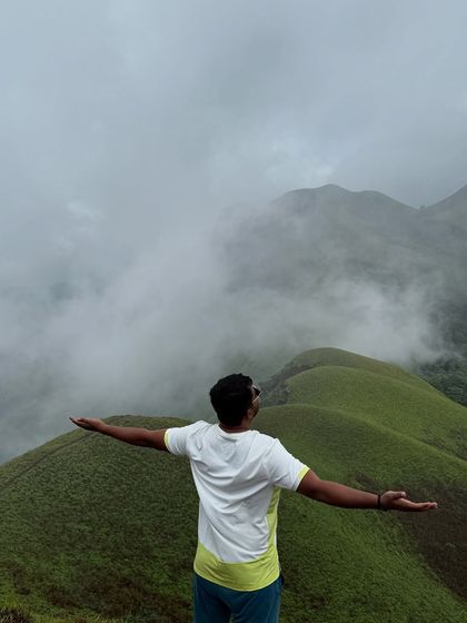 A trekker with arms outstretched, embracing the freedom and vastness of the Netravathi landscape.