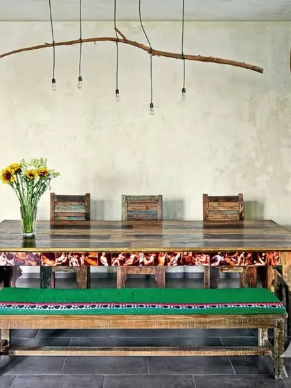 This eclectic dining room for Kangana Ranaut features a rustic wooden table with a bench, and a unique chandelier made from a tree branch. The walls are adorned with collected plates and a screen painted with portraits of Frida Kahlo, reflecting a truly artistic and bohemian spirit.