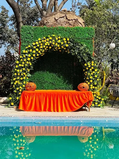 A poolside Haldi setup, using a green wall and yellow flower arch to create a fresh, natural look that complements the water.
