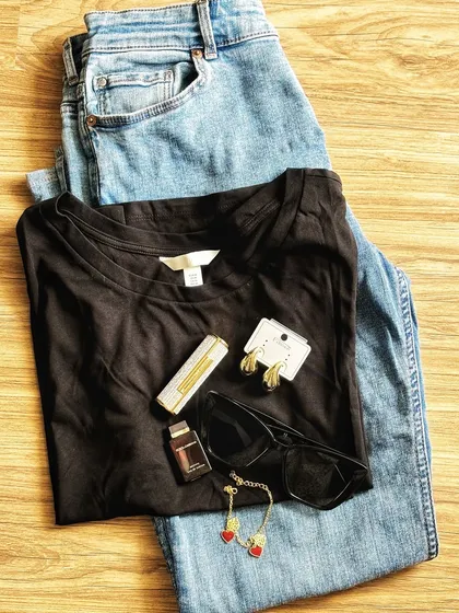 A classic outfit flatlay of a black t-shirt, blue jeans, and accessories. This is a simple yet effective way to showcase a complete look and individual product details.