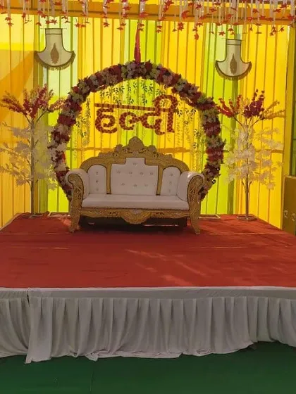 A traditional Haldi stage setup in Mumbai with a yellow and gold theme. The design includes a comfortable sofa for the couple and is flanked by sound systems for music and entertainment.