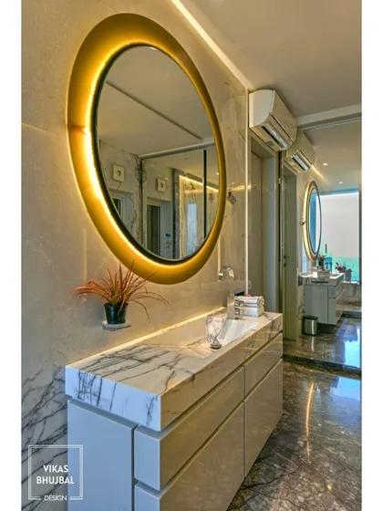 A backlit round mirror serves as the centerpiece of this vanity area. The marble countertop and sleek cabinetry provide ample storage, combining functionality with high-end design.