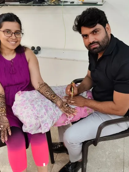 A photo of me applying mehandi to a client, who is smiling as she sees her design come to life.