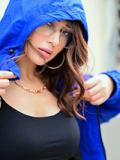A close-up of Mimi in a hooded jacket. The composition draws attention to her face and the cool, oversized glasses, creating an edgy and fashionable look.