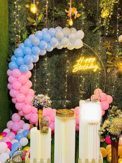 A beautiful garden-themed birthday setup with a pink and blue balloon arch, fairy lights, and decorative pillars.