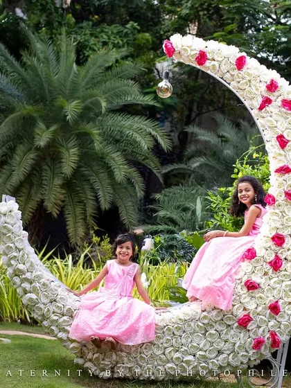 Childhood is a fairytale, and I love creating scenes to match. These two sisters are sharing a moment on a custom-made floral moon prop in a beautiful garden setting. A whimsical sibling photoshoot like this is a wonderful way to celebrate their unique bond.