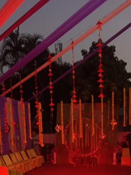 An outdoor evening setup with colorful drapes and hanging marigold strings. The lighting creates a warm and festive glow, perfect for a Sangeet or Mehandi party.