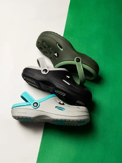 A creative composition of three pairs of clogs on a split green and white background. The diagonal arrangement is dynamic and visually interesting, making the product pop.