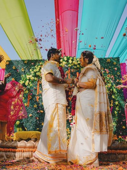 A beautiful moment from a South Indian wedding ceremony, with family showering the couple with flowers under a colorful canopy.