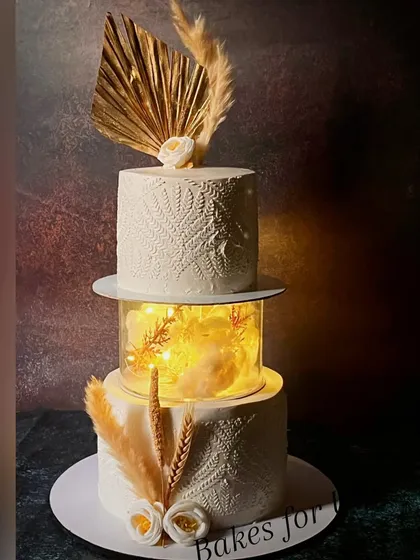 A sophisticated two-tier cake for a 40th birthday party, featuring an illuminated separator tier and elegant white stenciling. The dried floral arrangements add a modern, rustic touch.