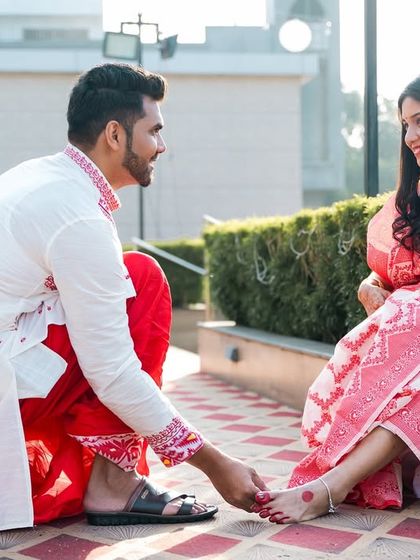 The groom applies alta on the bride's feet, a traditional Bengali pre-wedding custom filled with love.