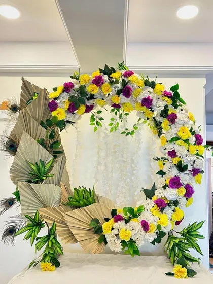 This design is a fusion of styles, mixing colorful flowers with dried palm leaves and peacock feathers for a modern, eclectic Ganpati decor.
