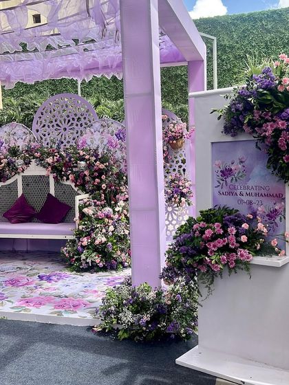 A dreamy pastel Haldi setup in shades of lavender. This unconventional design features intricate jaali panels, a floral-printed floor, and lush arrangements of purple and pink flowers for a unique and modern celebration.