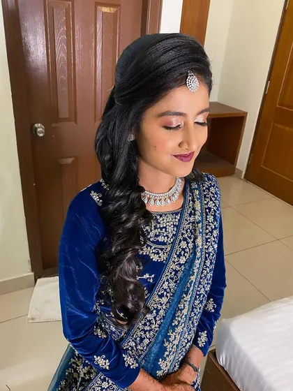 A bride ready for her reception in a stunning blue velvet lehenga. Her hair is styled in a side-swept look with soft curls, a glamorous and elegant choice.