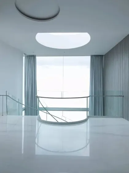 A serene, minimalist space featuring a circular skylight and floor-to-ceiling grey curtains, demonstrating how emptiness and light can be used to create a sense of calm and inertia.