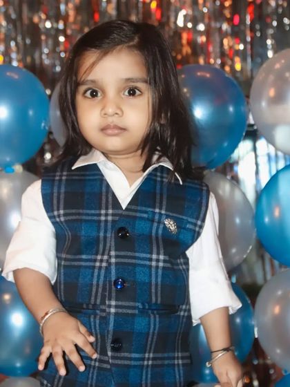 A young boy with long hair, dressed smartly in a plaid vest, poses for a portrait.
