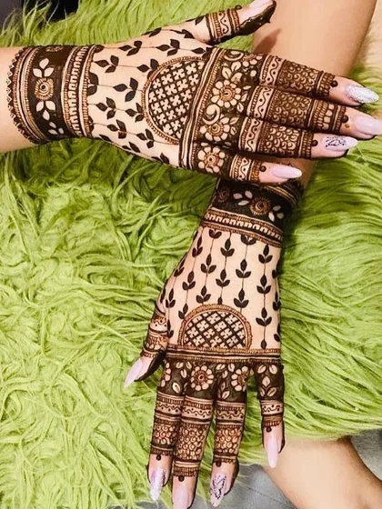 A happy client showing off her beautiful back-hand mehendi. The design features leafy vines and floral bands, with a rich, dark stain.