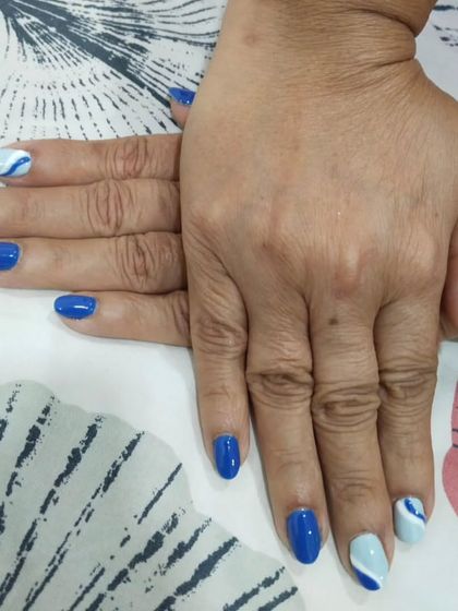 A bold blue manicure with a mix of solid royal blue and a light blue and white wave pattern on the accent nails. This is a fun, nautical-inspired look.