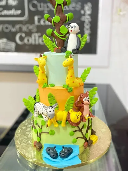 A grand three-tiered jungle adventure cake. Each tier represents a different part of the jungle, with animals like hippos, monkeys, lions, and a panda.