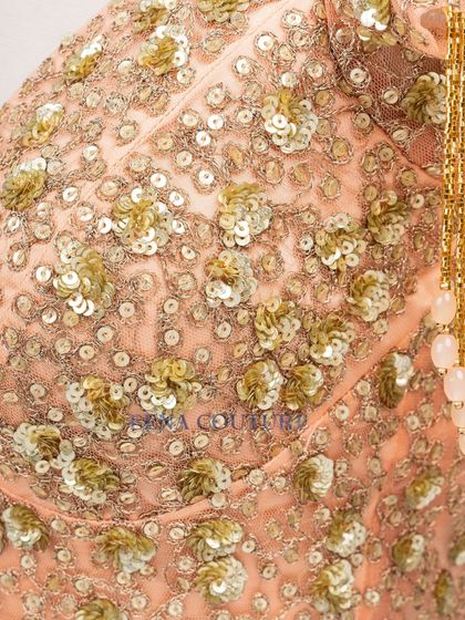 This peach-toned blouse is all about the sparkle and movement. It's crafted from net and covered in sequin and zardozi floral motifs, with dramatic, dangling beaded tassels on the sleeves for a show-stopping effect.